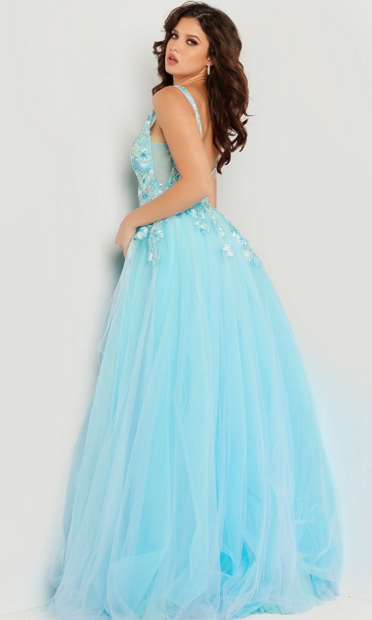 A woman stands against a light background, looking over her shoulder in the Jovani Long Turquoise Prom Ball Gown 26045 with embroidered flowers.